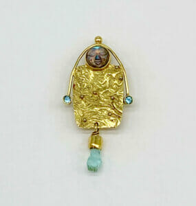 Pin with carved moon face, a natural aquamarine crystal, and aquamarines has gold bezels
