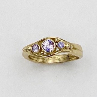 This sweet little split shank 18k yellow gold ring has a unique .28 ct. pastel parti-colored sapphire (H) in the center with pastel purple sapphires (H) on either side.