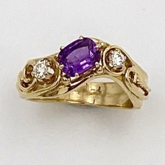 18k yellow gold ring with a 1.22 ct. cushion cut natural color purple sapphire flanked by .15 ct. ideal cut, "E" color, VS clarity diamonds. Prong settings for the gems are 14k yellow gold.