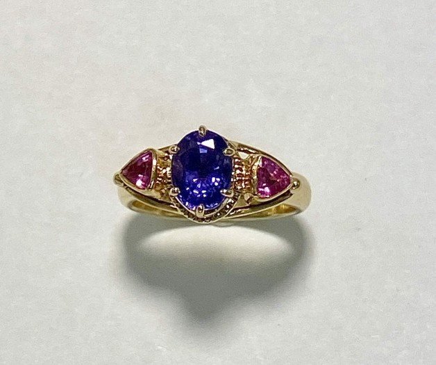 The stunning center stone in this 18k yellow gold ring is a 2.50 ct. natural color purple sapphire and is flanked by two hot pink trillion sapphires (H).