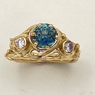 18k yellow gold ring with a teal color Montana sapphire (H) weighing 1.47cts. and flanked by .29ct.(TW) diamonds, E Color, VS clarity