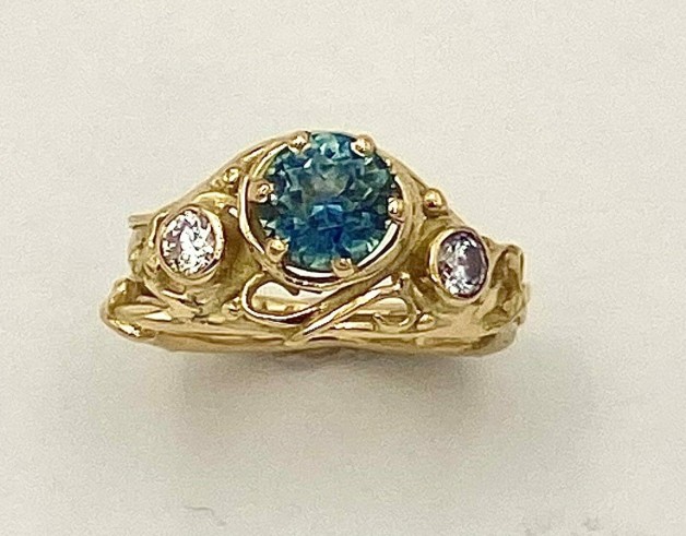 18k yellow gold ring with a teal color Montana sapphire (H) weighing 1.47cts. and flanked by .29ct.(TW) diamonds, E Color, VS clarity